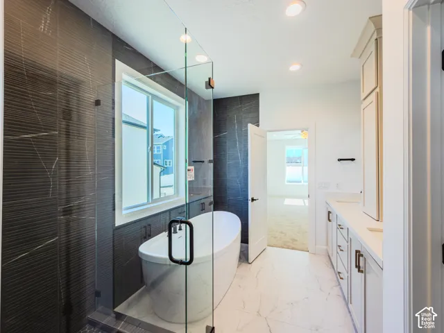 Freestanding soaking tub, floor-to-ceiling dark textured tile surround, glass-enclosed shower, dual-sink vanity with light cabinetry, and light-toned tile flooring