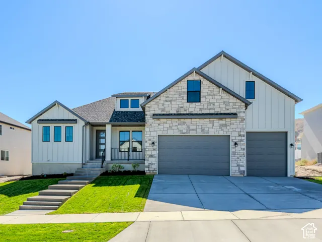 Modern two-story exterior featuring vertical siding, stone masonry accents, a three-car garage, and concrete staircase leading to a covered entry