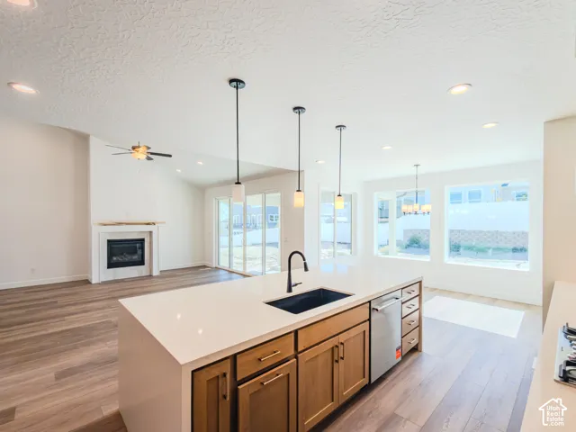 Kitchen island featuring a quartz countertop, under-mount sink, and matte black faucet, complemented by wood-finish cabinetry, recessed lighting, and pendant fixtures