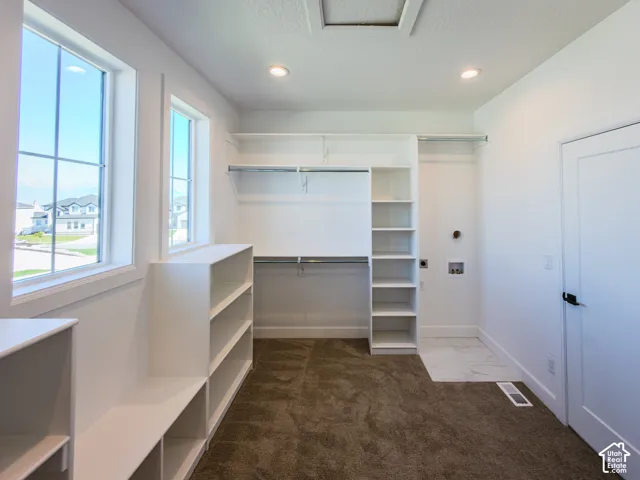 Walk-in closet featuring white built-in shelving, dual hanging rods, recessed lighting, and designated tile floor area for utility connections