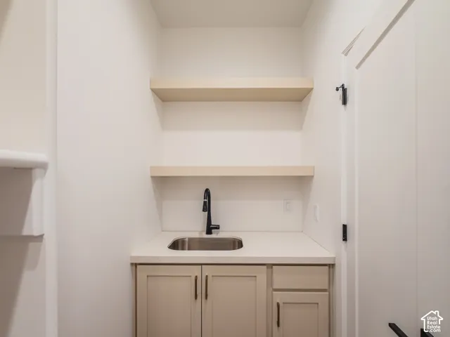 Built-in wet bar featuring custom cabinetry, solid-surface countertops, an undermount sink with a matte black faucet, and dual floating shelves