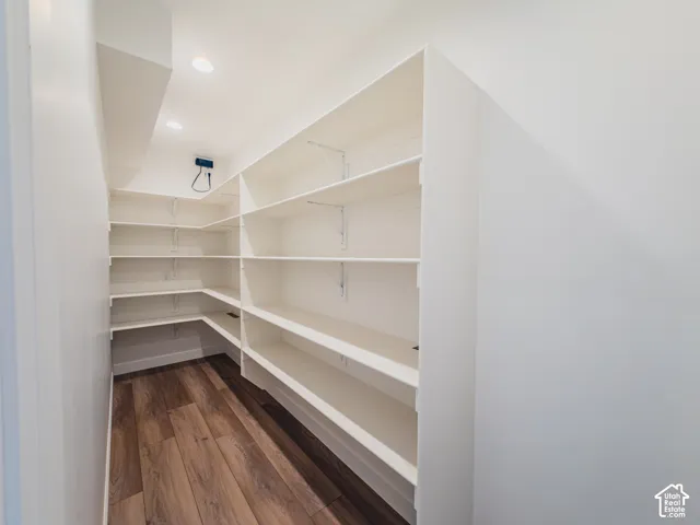 Walk-in storage space featuring multi-tier shelving, recessed ceiling lighting, and wood-finish flooring