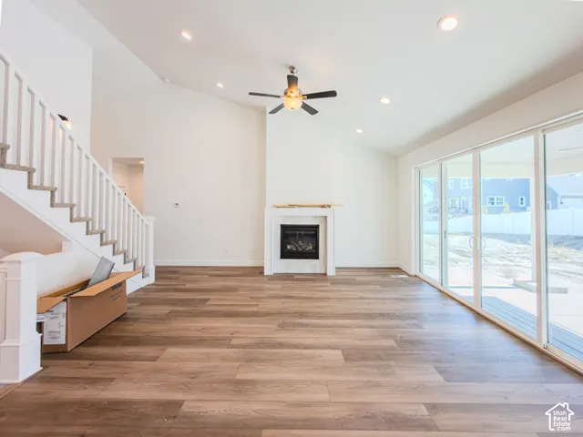 Vaulted ceilings featuring recessed lighting and a central ceiling fan, wood-finish flooring, fireplace with a mantel, and sliding glass doors