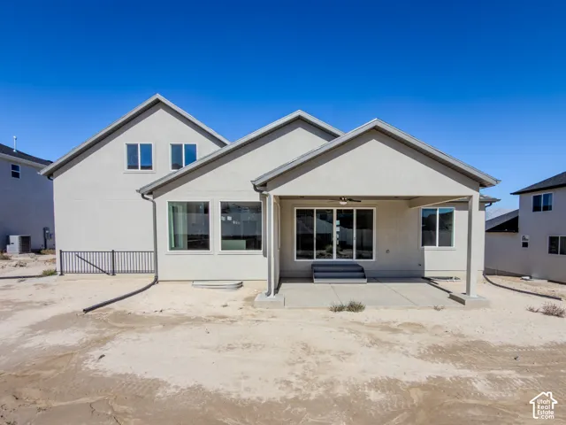 Exterior featuring a multi-gabled roofline, light-toned stucco siding, a concrete rear patio, and a metal perimeter fence