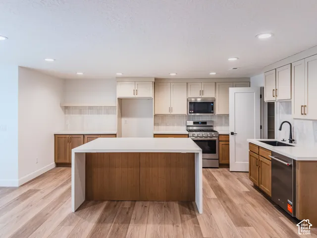 Kitchen featuring a central island with waterfall-edge stone countertop, two-tone cabinetry, recessed lighting, and stainless steel appliances
