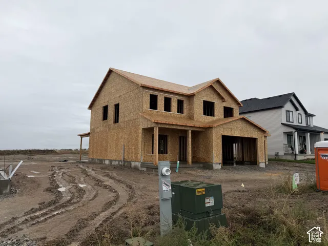 Two-story residential structure under construction featuring oriented strand board exterior sheathing, a gabled roofline, a covered front entry porch, and a multi-car garage frame