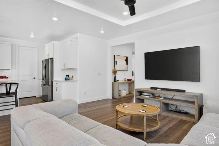 Tray ceiling with recessed lighting, wood-finish flooring, white cabinetry, and stainless steel refrigerator