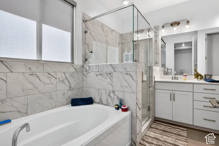 Deep soaking tub, walk-in glass-enclosed shower, stone-pattern tile surrounds, white cabinetry, and vanity with integrated sink