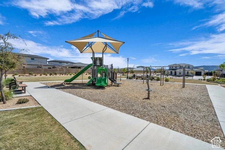 Community recreation area featuring a multi-level playground structure with a shade canopy, swing set, concrete walking paths, and built-in metal seating