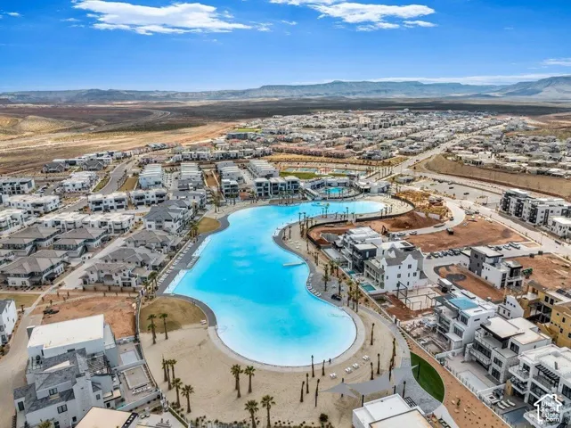 Aerial perspective of a master-planned community featuring an expansive lagoon-style recreational pool, sand beach border, palm landscaping, and mountain backdrop