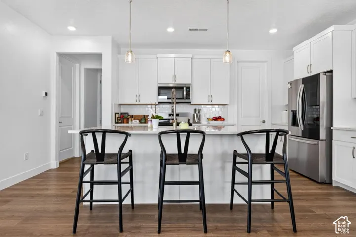 Kitchen featuring white cabinetry, quartz countertops, a subway tile backsplash, stainless steel appliances, and wood-finish flooring