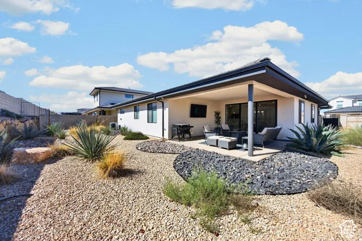 Covered rear patio featuring a concrete slab foundation, xeriscaped grounds with decorative rock beds, and large-leafed agave plantings
