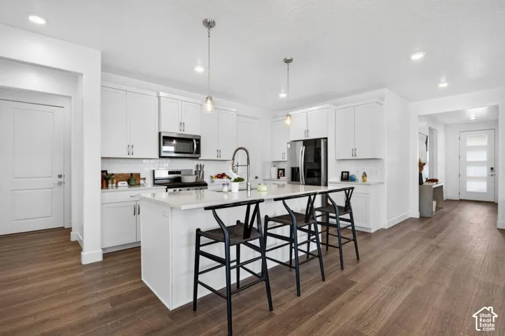 Kitchen featuring white shaker-style cabinetry, a central island with quartz countertops, stainless steel appliances, recessed lighting, and wood-finish flooring