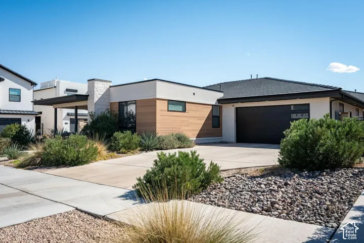 Modern exterior featuring stucco finish, wood-finish paneling, stone chimney accent, dual-car garage, and desert-style landscaping