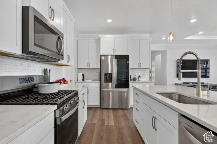 Kitchen featuring white shaker-style cabinetry, stainless steel appliances, a central island with a stainless steel sink, quartz countertops, and wood-finish flooring