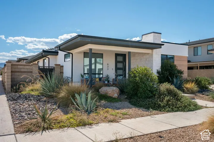 Modern single-story exterior featuring a flat roofline, neutral stucco siding, natural stone accents, and desert-inspired landscaping