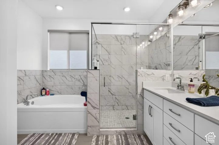 Bathroom featuring a deep soaking tub, glass-enclosed walk-in shower with stone-patterned tile surround, white cabinetry, solid-surface countertop, and dual-basin vanity