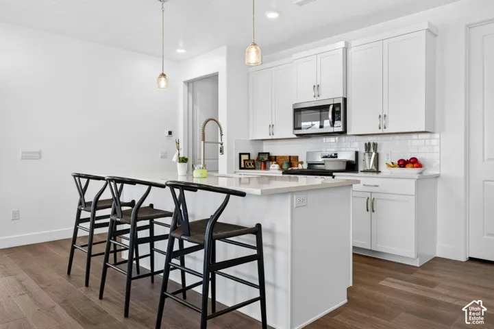 Kitchen featuring white shaker-style cabinetry, quartz countertops, subway tile backsplash, stainless steel built-in microwave, and wood-finish flooring