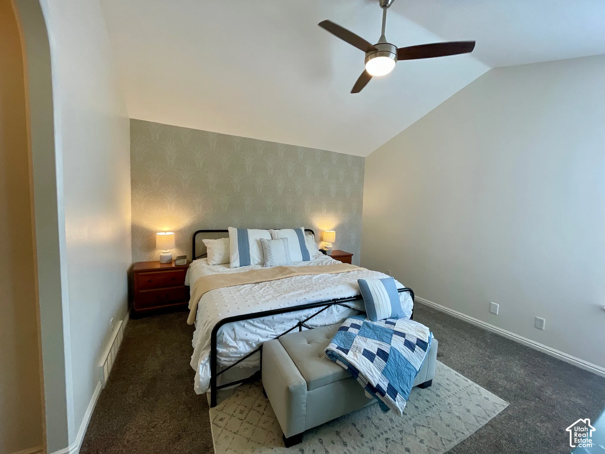 Vaulted ceiling with a central multi-blade ceiling fan and an accent wall featuring patterned wall covering