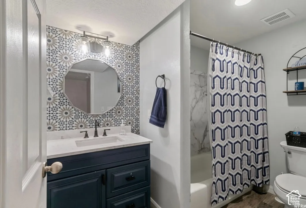 Bathroom featuring a navy vanity with a stone countertop, an integrated sink, a geometric patterned feature wall, and a shower-tub combination with stone-patterned surround