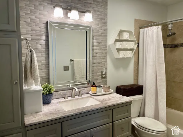 Vanity featuring a stone-look countertop, integrated rectangular sink, and gray shaker-style cabinetry with a stacked-stone textured wall accent