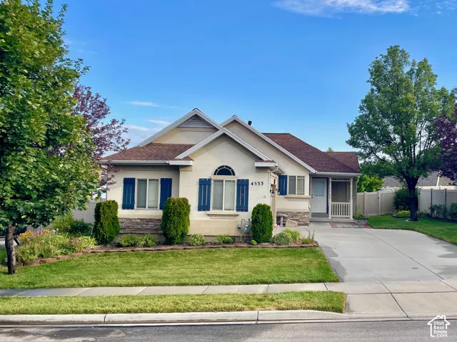 Stucco and stone veneer exterior featuring an arched window, decorative shutters, a concrete driveway, and a covered entryway