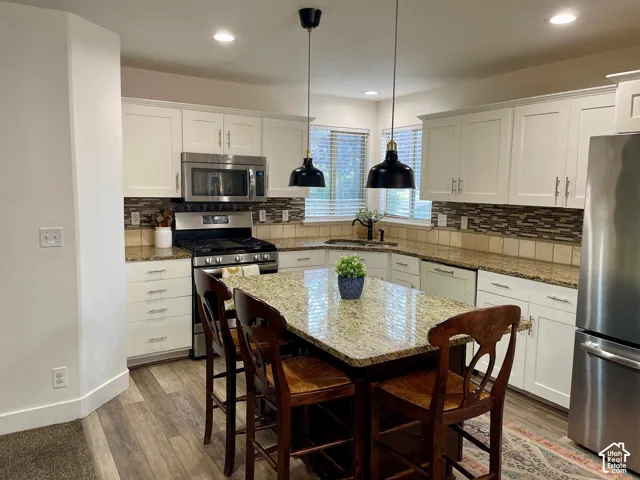 Kitchen featuring white cabinetry, stone-surface countertops, tile backsplash, stainless steel appliances, and a central island with dual pendant lighting
