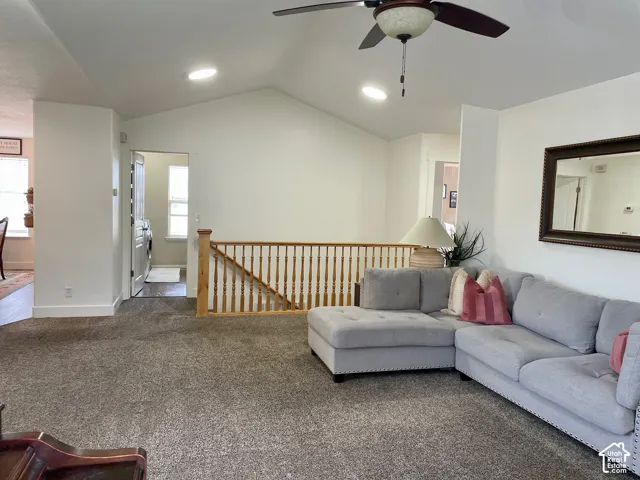 Vaulted ceilings, neutral carpeting, wooden spindle railing, and ceiling-mounted light fixture