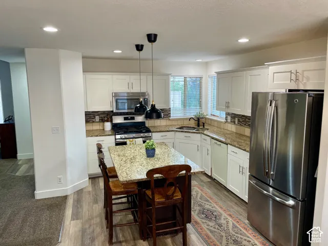 Kitchen featuring white shaker-style cabinetry, stone countertops, central island, stainless steel appliances, and dual pendant lighting
