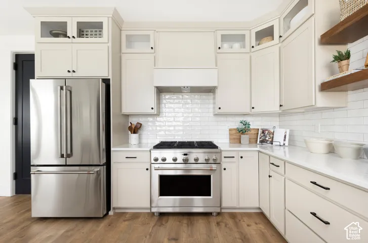 Stainless steel refrigerator and range, white subway tile backsplash, light cabinetry with dark hardware, and wood-finish flooring