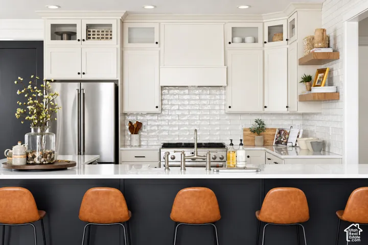 Kitchen featuring white shaker-style cabinetry, a built-in stainless steel refrigerator, white subway tile backsplash, a stainless steel gas range, and a kitchen island with a white countertop