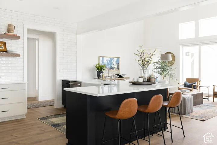 Kitchen featuring a large island with white countertops, wood-finish flooring, white brick-patterned wall tiles, and white shaker-style cabinetry