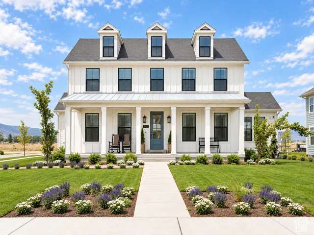 White board and batten exterior, covered front porch, dark-framed windows, dormer windows, and a manicured lawn with planted flower beds