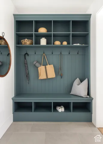 Built-in storage unit with open shelving and lower cubbies, featuring beadboard paneling, a seating bench, and multiple coat hooks