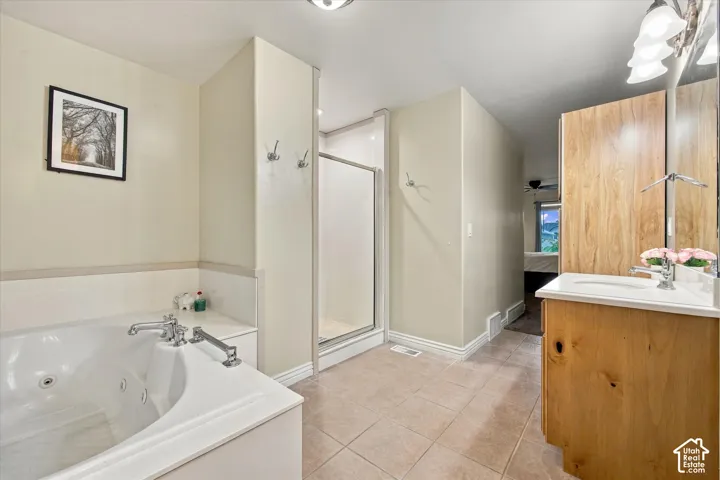 Jetted soaking tub with tile surround, wood-finish cabinetry, ceramic tile flooring, enclosed glass shower, and wall-mounted metal hardware