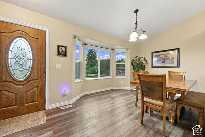 Solid wood entry door with oval decorative glass insert, bay window, and wood-finish flooring, illuminated by a multi-light chandelier