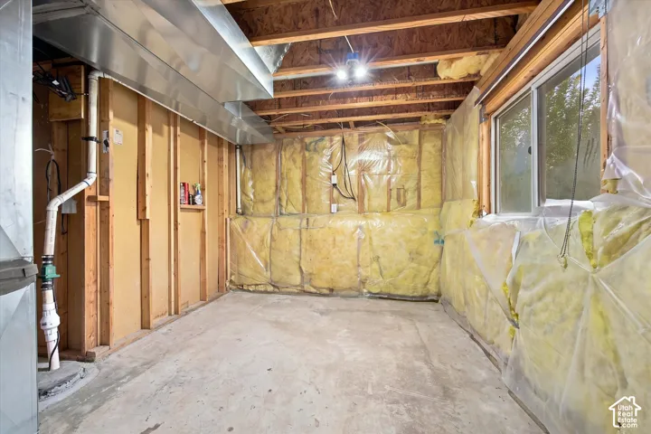 Unfinished interior space featuring exposed wood framing, batt insulation with a plastic vapor barrier, concrete flooring, and metal ductwork