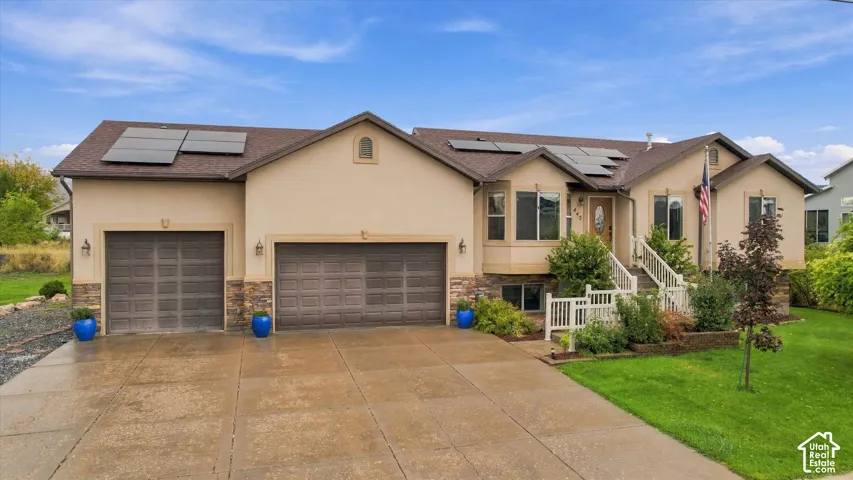 Stucco and stone facade featuring a three-car garage, roof-mounted solar panels, and raised entry porch with white railings