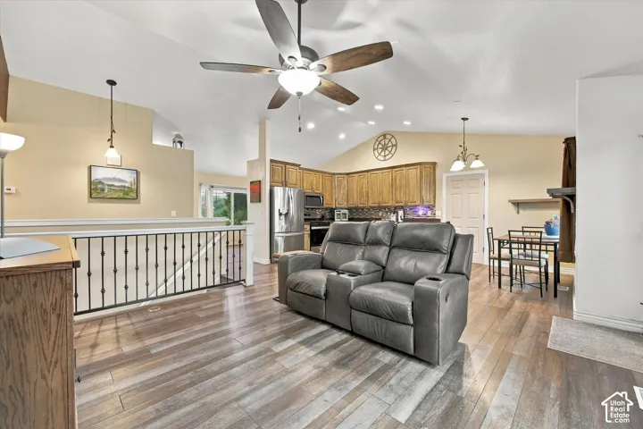 Open-concept living space with vaulted ceilings, wood-finish flooring, metal spindle railing, ceiling fan with light fixture, and kitchen cabinetry