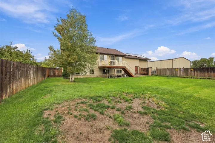 Expansive backyard featuring a wood-railed deck, mature trees, wood privacy fencing, and an auxiliary metal structure