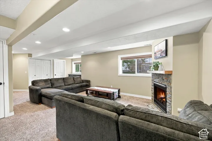 Living space featuring a stone-faced fireplace with a wood mantel, recessed lighting, carpeted flooring, and dual-door closets
