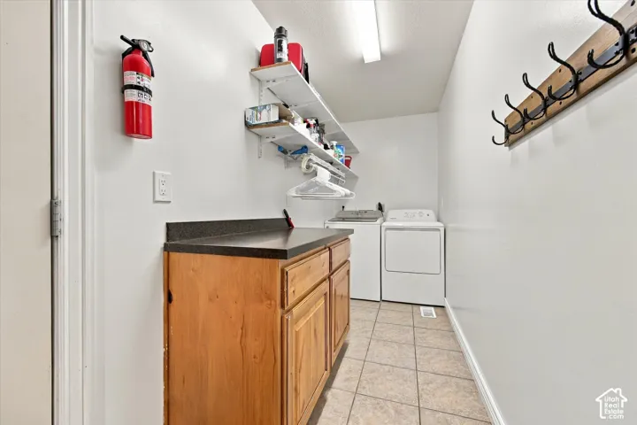 Laundry area featuring tile flooring, built-in wooden cabinetry with a dark countertop, white wall-mounted shelving, and a wall-mounted hook rack
