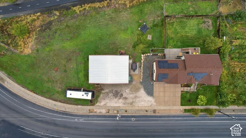 Aerial view featuring a spacious lot with a detached metal-sided workshop, rooftop solar panel array, concrete driveway, and landscaped grounds