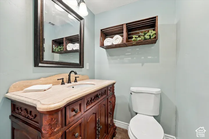 Custom wood vanity featuring intricate carvings, stone-finish countertop with an undermount sink, dark-finish widespread faucet, framed wall mirror, and wall-mounted wooden crate shelving