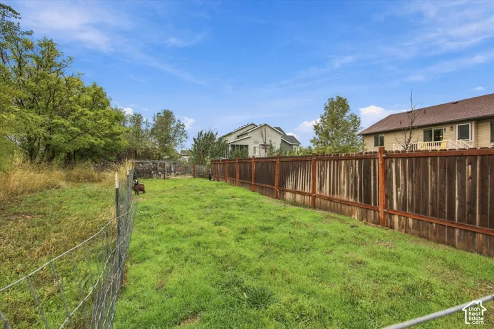 Expansive backyard featuring a wood privacy fence, wire mesh perimeter fencing, and mature trees