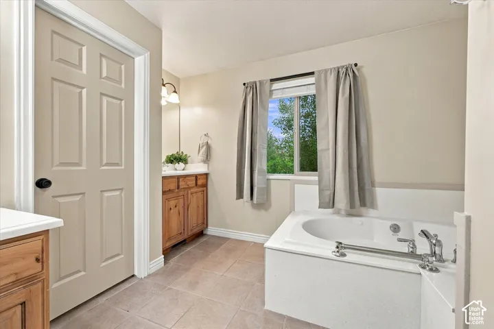 Bathroom featuring a deep-basin soaking tub with a tiled surround, wood-finish cabinetry, neutral tile flooring, and a window with natural light