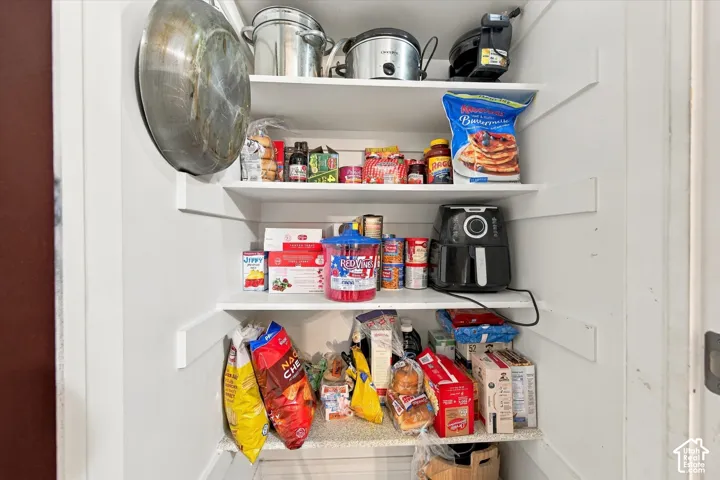Pantry storage featuring white painted wooden shelving and solid surface shelving base