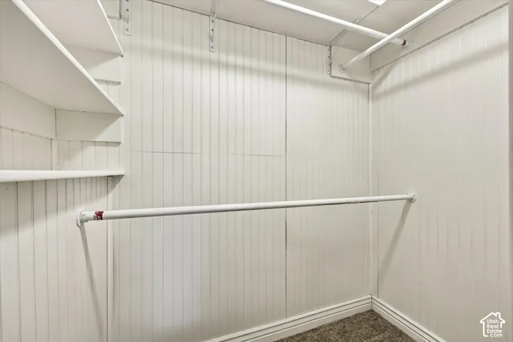 Storage space featuring white beadboard wall paneling, built-in shelving units, and dual-level metal hanging rods