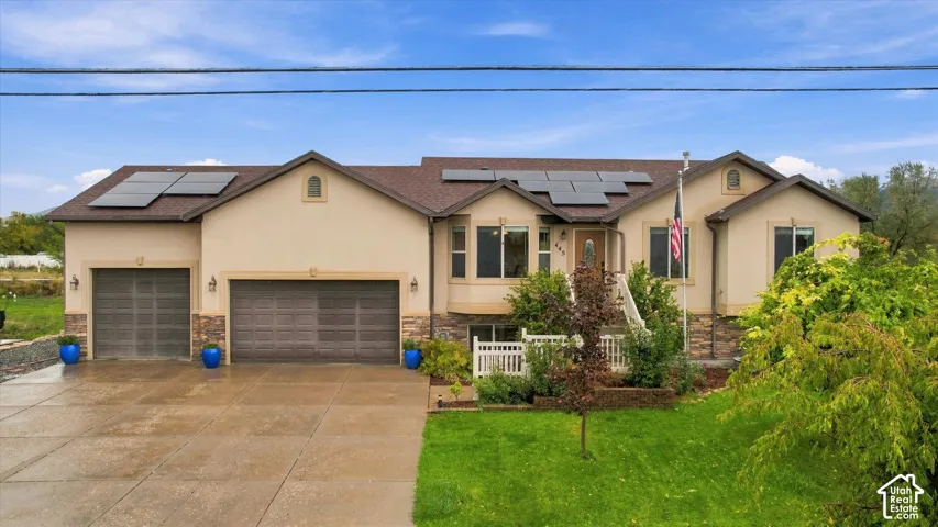 Single-story residence featuring a multi-car garage, stone veneer siding, rooftop solar panels, and a concrete driveway