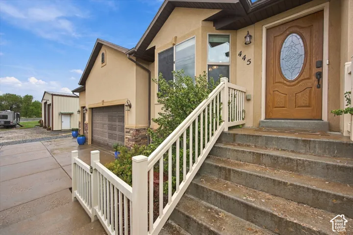 Exterior featuring stucco siding with stone veneer accents, an arched front door with decorative glass inlay, concrete stairs with white balustrade railing, a multi-car garage, and a detached outbuilding